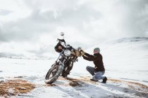 Side view of man arranging motorcycle while traveling at snowy mountains valley. — Stock Photo