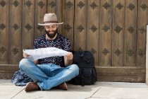 Bearded man in hat sitting by gates and reading map — Stock Photo
