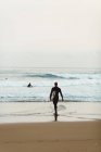 Vista trasera del hombre surfista caminando en la playa - foto de stock