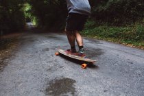 Обрізаний чоловік на скейтборді їде по лісовій дорозі — стокове фото