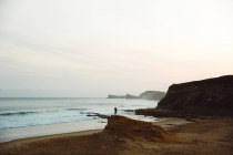 Vista à distância do homem posando no penhasco costeiro contra a paisagem marinha — Fotografia de Stock