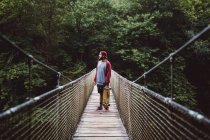 Side view of man with skateboard posing on forest rope bridge — Stock Photo
