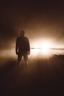 Rear view of male silhouette posing against light at brown mist. — Stock Photo