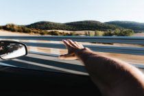 Crop male hand sticking out of window while driving along highway through prairie. — Stock Photo