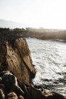 Віддалений вигляд людини, що стоїть на береговій скелі над жорстким морем — стокове фото