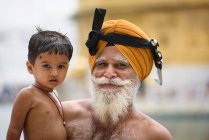 Lächelnder erwachsener Mann mit Bart hält indischen Jungen auf Händen. — Stockfoto
