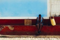 CUBA - AUGUST 27, 2016: Front view of man sitting on shabby fence at street scene — Stock Photo