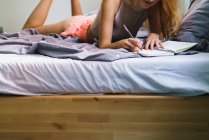 Обрізати жінку лежить на ліжку і пише в блокноті — стокове фото