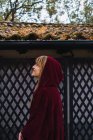 Vue latérale de la fille brune portant une veste à capuche rouge posant contre une clôture au parc — Photo de stock