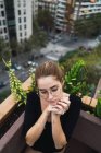 High angle view of brunette girl in eyeglasses posing with hands near chin at terrace — Stock Photo