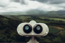 Panoramic view of green valley and sight-seen binoculars under cloudy sky. — Stock Photo