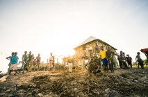 BENIN, ÁFRICA - 31 de agosto de 2017: Grupo de negros posando alrededor de una casa de paja pobre en la zona tropical . - foto de stock