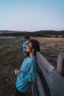 Vista lateral da menina em camisola azul inclinada na cerca no campo — Fotografia de Stock