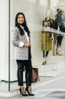 Ritratto a figura intera di donna che indossa tuta posa vicino alla vetrina del negozio — Foto stock