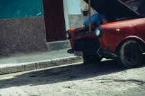 CUBA - 27 DE AGOSTO DE 2016: Vista inclinada del hombre doblando y reparando el motor en el coche viejo en la calle . - foto de stock