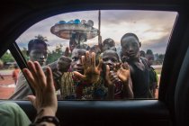 BENIN, ÁFRICA - 31 DE AGOSTO DE 2017: Gestos de la mano de las cosechas a un grupo de niños africanos fuera del automóvil . - foto de stock