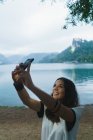 Sorridente bruna donna prendere selfie a riva del lago — Foto stock