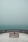 Chien assis derrière le banc sur la terrasse sur fond de paysage marin brumeux — Photo de stock