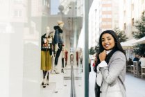 Retrato de mulher sorridente vestindo jaqueta posando perto da vitrine — Fotografia de Stock