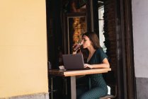 Вид сбоку женщины, пьющей кокс за ноутбуком на столе в кафе — стоковое фото