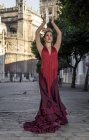 Bailarina de flamenco vestida de traje nacional posando en plaza de la ciudad con los brazos levantados - foto de stock