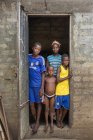 BENIN, ÁFRICA - 31 de agosto de 2017: Retrato de la madre con los niños de pie en la puerta de entrada en casa y mirando a la cámara . - foto de stock
