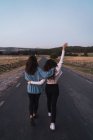 Visão traseira de duas mulheres abraçando umas às outras e andando ao longo da estrada rural . — Fotografia de Stock