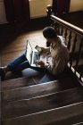 Человек сидит на лестнице с ноутбуком на коленях и просматривает смартфон — стоковое фото