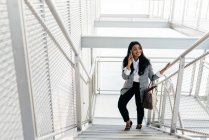Елегантна бізнес-леді розмовляє зі смартфоном і сходження сходами — стокове фото