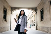 Low angle portrait of elegant businesswoman posing with phone at street archway — Stock Photo