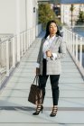 Stylische Geschäftsfrau in Jacke posiert auf sonnenbeschienener Balkonpassage — Stockfoto