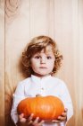 Adorable child posing with pumpkin by wooden wall — Stock Photo