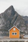 Cabin on lake shore over Mountain cliff on background — Stock Photo