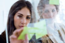 Portrait of business woman sticking note on glass in office. — Stock Photo