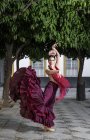Flamenco dancer wearing red dress posing over trees at street scene — Stock Photo