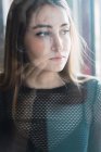 Portrait of young girl with piercing posing pensively behind glass and looking away sadly — Stock Photo