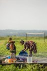 BENIN, AFRICA - AUGUST 31, 2017: Side view of black ethnic woman washing utensils at water point on background of tropics. — Stock Photo