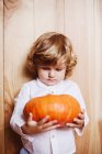 Adorable boy looking at pumpkin by wooden wall — Stock Photo