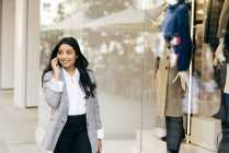 Portrait of businesswoman walking along shop windows and talking phone — Stock Photo