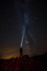 Rückansicht von Person, die auf Klippe steht und Beleuchtung mit Taschenlampe zur Milchstraße — Stockfoto