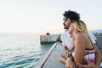 Side view of embracing couple and looking at ocean landscape in twilight. — Stock Photo