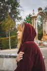 Side view of brunette girl in red hood posing over arch statue on background — Stock Photo