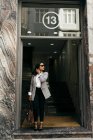Retrato de mulher de negócios elegante em óculos de sol saindo do prédio e olhando para o lado — Fotografia de Stock