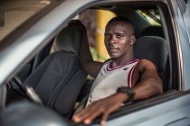 BENIN, ÁFRICA - 31 de agosto de 2017: Retrato del hombre sentado en el coche en el lugar del conductor y mirando a la cámara . - foto de stock