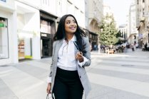 Retrato de una elegante mujer de negocios sonriente caminando por la calle y mirando a un lado - foto de stock