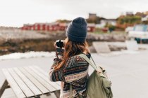 Rear view of woman with backpack taking shots on camera in hands — Stock Photo