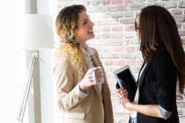 Side view of two businesswoman cheerfully talking at office. — Stock Photo