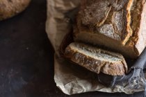 Blick von oben auf hausgemachtes Brot und Scheiben auf rustikalem Papier — Stockfoto