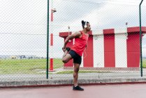 Vista lateral do desportista em fones de ouvido alongando a perna antes de correr — Fotografia de Stock