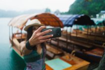 Retrato de una mujer tomando selfie cerca de barcos en el lago - foto de stock